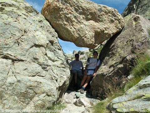 Two hikers sitting beneath a massive boulder wedged between granite rocks