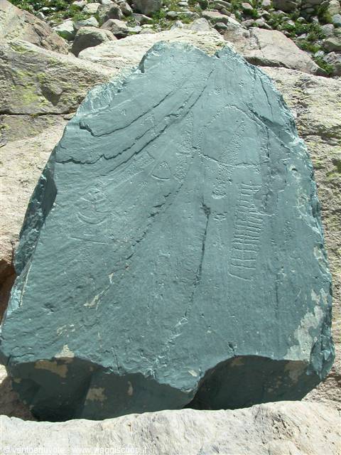Green boulder with rock carvings, surrounded by light stones, in sunlight