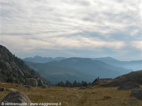 Blue mountains under clouds, stone hut and boulders in dry grass
