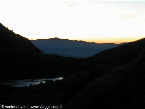 Mountains silhouetted at dawn, small dark lake among rocky slopes