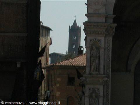 Brick bell tower between Siena buildings, marble statues in the foreground