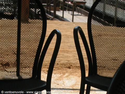 Black perforated metal chairs on a terrace, sunlit sand in background