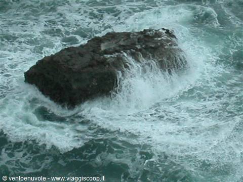 Dark rock surrounded by white foam of crashing waves