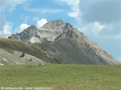 Grey rocky peaks above a green grassy slope, white clouds in the blue sky
