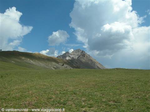 Green meadow under white clouds and rocky peaks of Mount Sirente