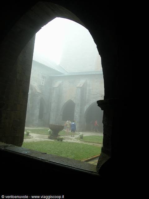 Foggy cloister seen through an arched window, tourists in the inner garden