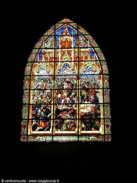 Gothic stained glass window with painted battle scenes glowing in dark church