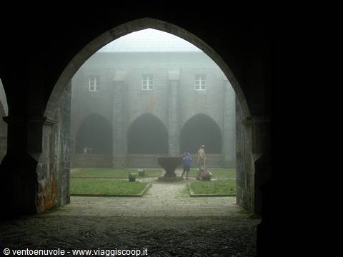 Stone cloister shrouded in fog, two people beside the central well