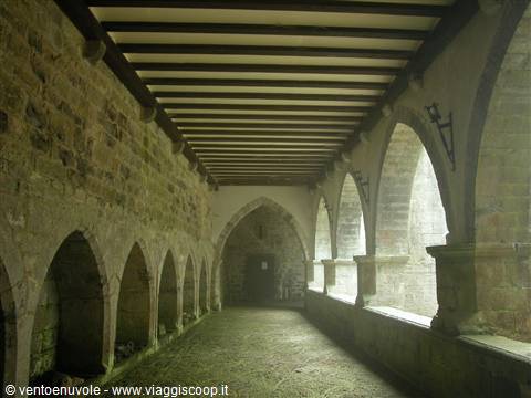 Stone cloister with Romanesque arches and beamed ceiling, soft light