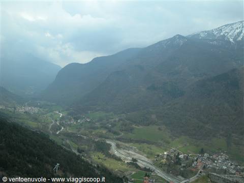 Villages and stream in a green valley between snowy cloudy mountains