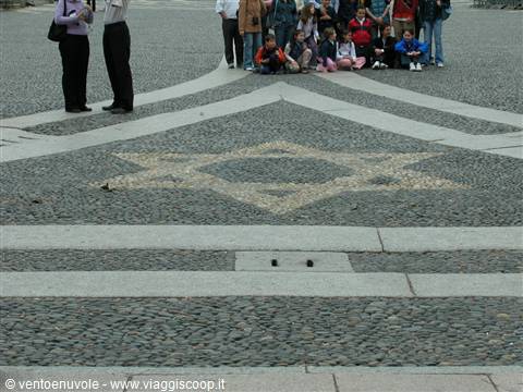 Star of David pattern in cobblestone pavement, group of visitors standing nearby