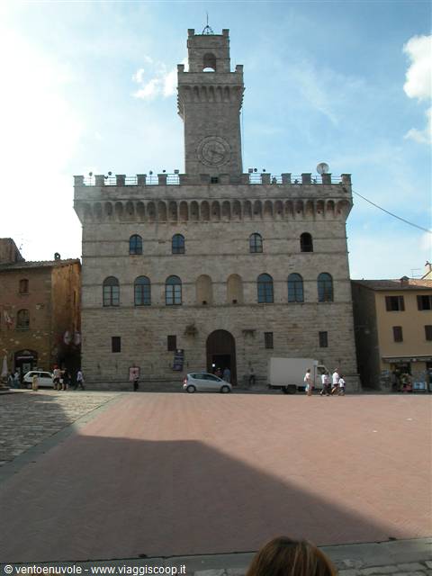 Montepulciano's Piazza Grande, stone town hall with crenellated tower, cars and passersby