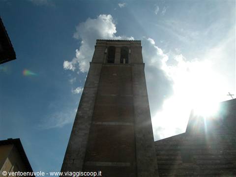 Romanesque stone bell tower seen from below, backlit against sunlit clouds