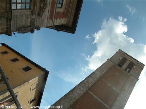 Stone and brick bell tower between old buildings, white clouds in blue sky