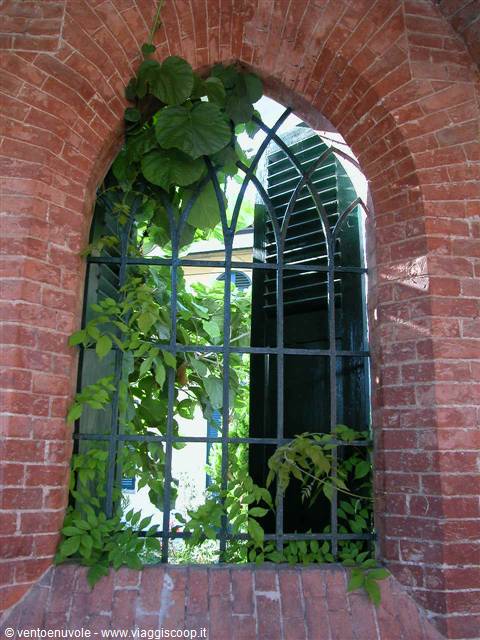 Arched red brick window with dark green iron grating and climbing vines