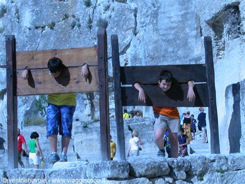 Children with head and hands locked in wooden stocks among white rocks