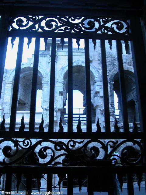 Wrought iron gate framing the stone arches of Arles Roman amphitheatre