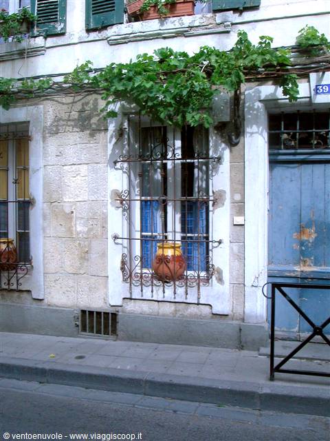 Stone facade with green shutters, wrought iron grilles and terracotta pot at the window