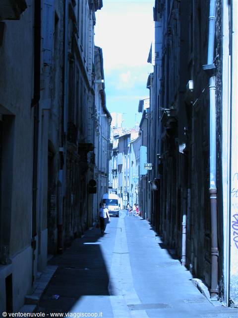 Pedestrian walks down a narrow alley between old facades, truck ahead