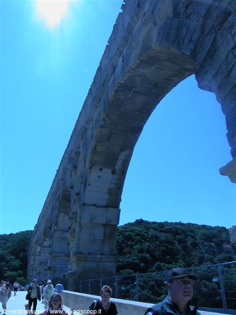 Tourists walk across the Pont du Gard, Roman stone aqueduct, under bright sun