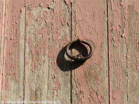 Rusty iron door knocker on weathered wood with peeling pink paint