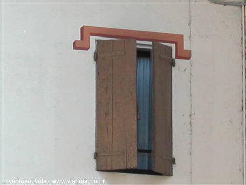 Window with open wooden shutters and a painted red frame on the wall