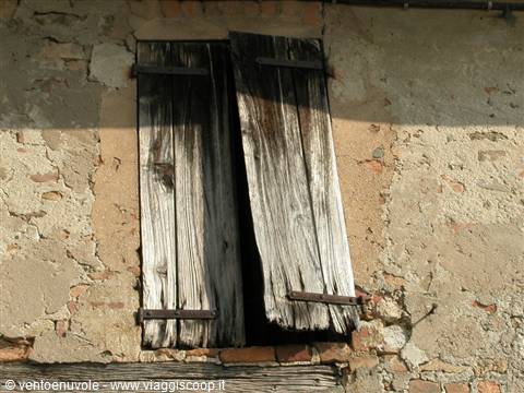 Old window with broken wooden shutters on a crumbling brick wall