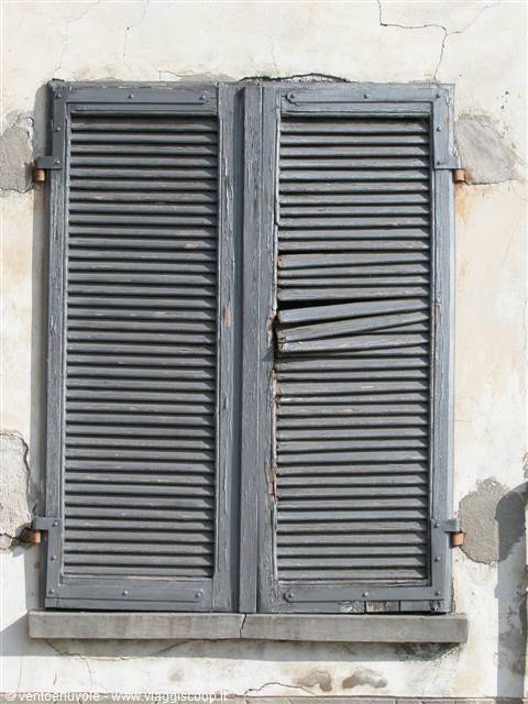 Old grey wooden shutters on cracked plaster wall, one slat broken