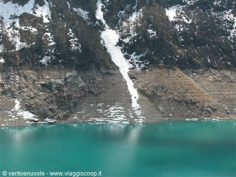 Turquoise lake beneath rocky slopes with patches of snow