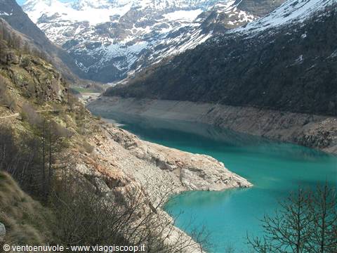 Turquoise reservoir surrounded by snowy peaks, rocky shores and sparse woods