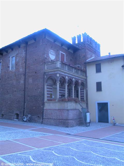 Brick palace with arched loggia and crenellated tower, paved square, parked bicycle