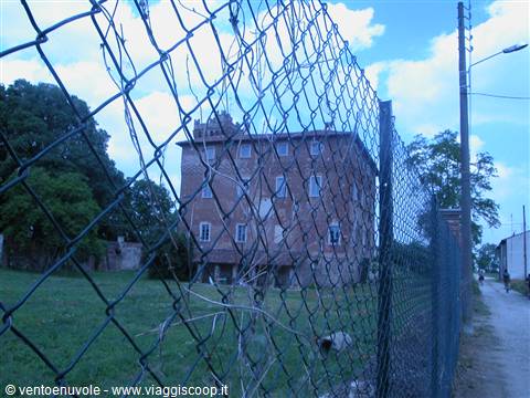 Brick building behind a chain-link fence, blue sky and dirt road