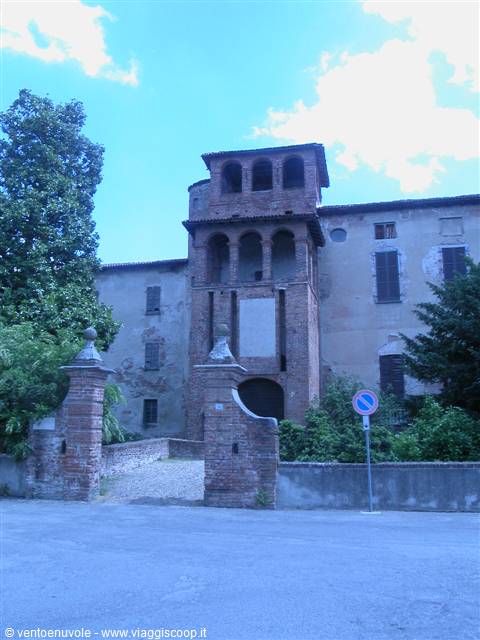 Ancient brick castle with arched tower among trees under blue sky