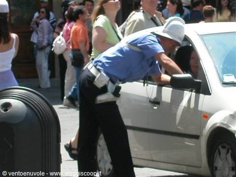 Traffic officer in white helmet leans into a white car on a busy street