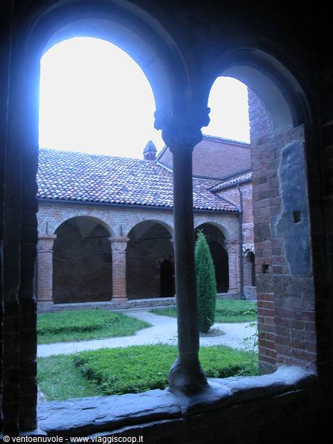 Brick cloister with arcade and grassy courtyard seen through medieval double arch
