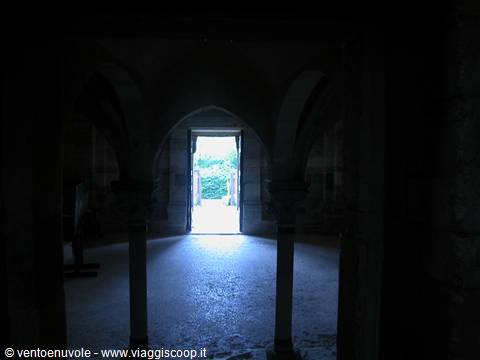 Stone columns and gothic arches in shadow, daylight pouring through open doorway