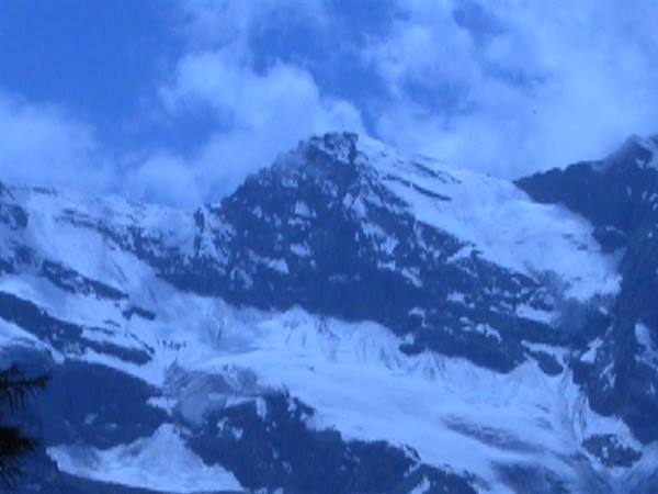 Snowy rocky peaks under white clouds in blue light