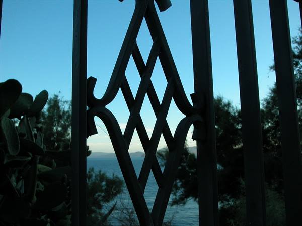 Black wrought iron scroll frames the sea and trees at dusk