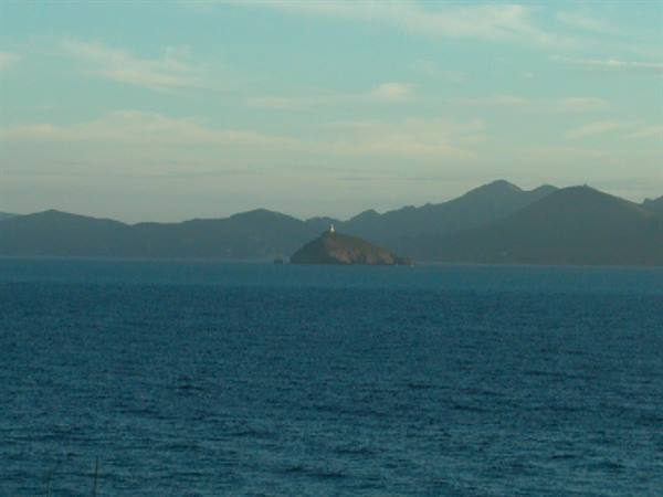 Rocky islet with lighthouse in the middle of the sea, dark mountains behind