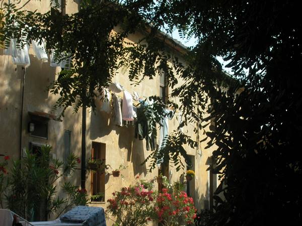 Laundry hanging among trees in front of a golden stone farmhouse