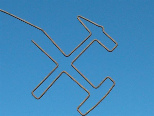 Metal sculpture of crossed hammers against blue sky