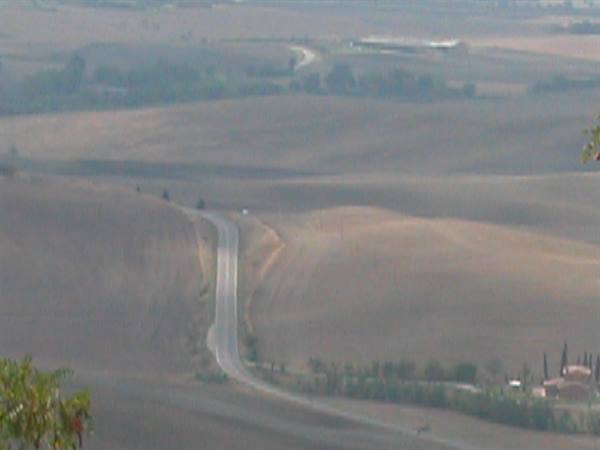 Winding road through cultivated rolling hills, farmhouse with cypress trees below