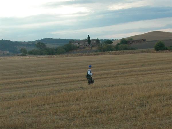 Hiker with backpack crossing a plowed field near Tuscan farmhouses