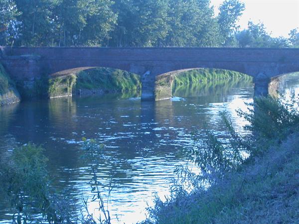 Old brick bridge with arches reflected in the river water