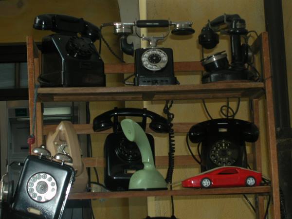 Old rotary telephones displayed on wooden shelves, including a green shoe-shaped one