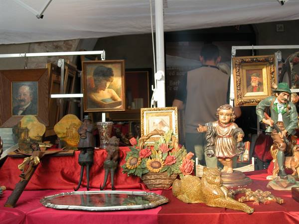Flea market stall with old paintings, wooden statues and dried flowers under white tent