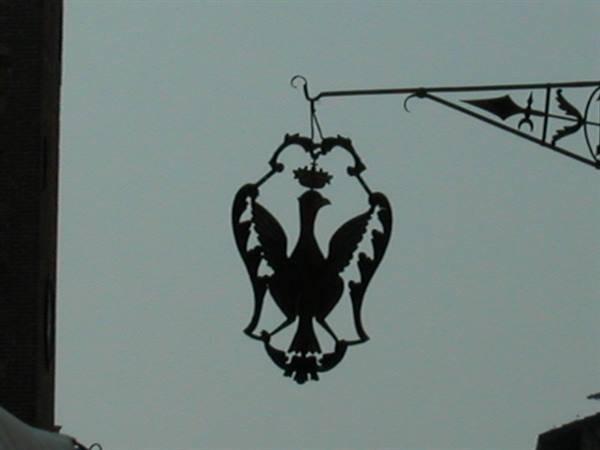 Wrought iron sign shaped like a crowned bird, dark silhouette against grey sky