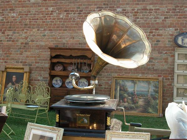 Antique gramophone with golden horn among paintings and furniture at flea market