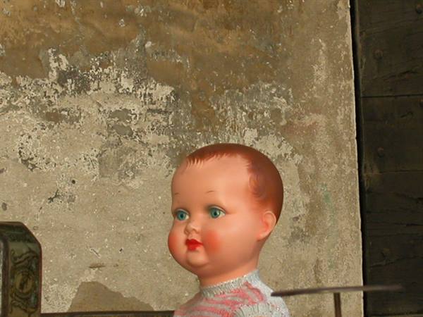 Plastic doll with green eyes against a weathered plaster wall