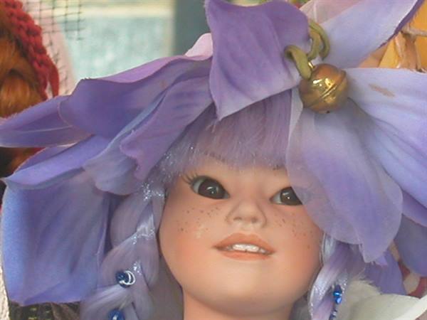 Doll with braided lilac hair wearing large purple flower hat with golden bell